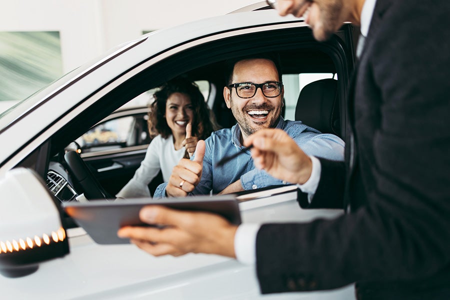 The salesperson is presenting the document to the customer while seated in the car.